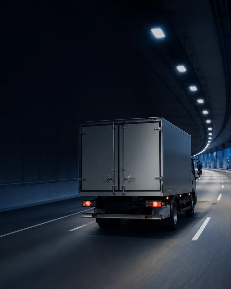 An unbranded cargo truck traveling through a lit city tunnel at night